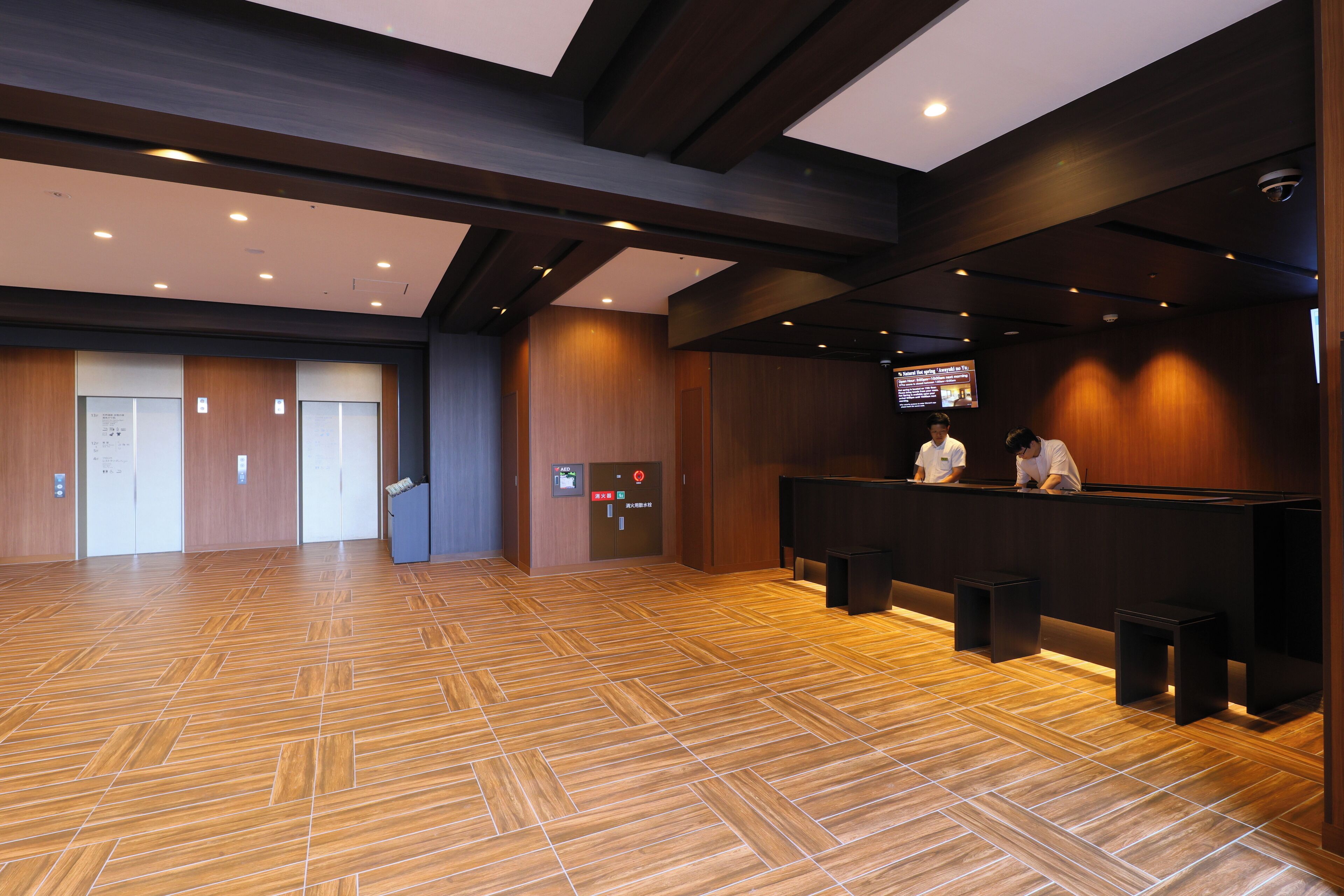 Zona de recepción con suelo de madera, mostrador de recepción y dos empleados.