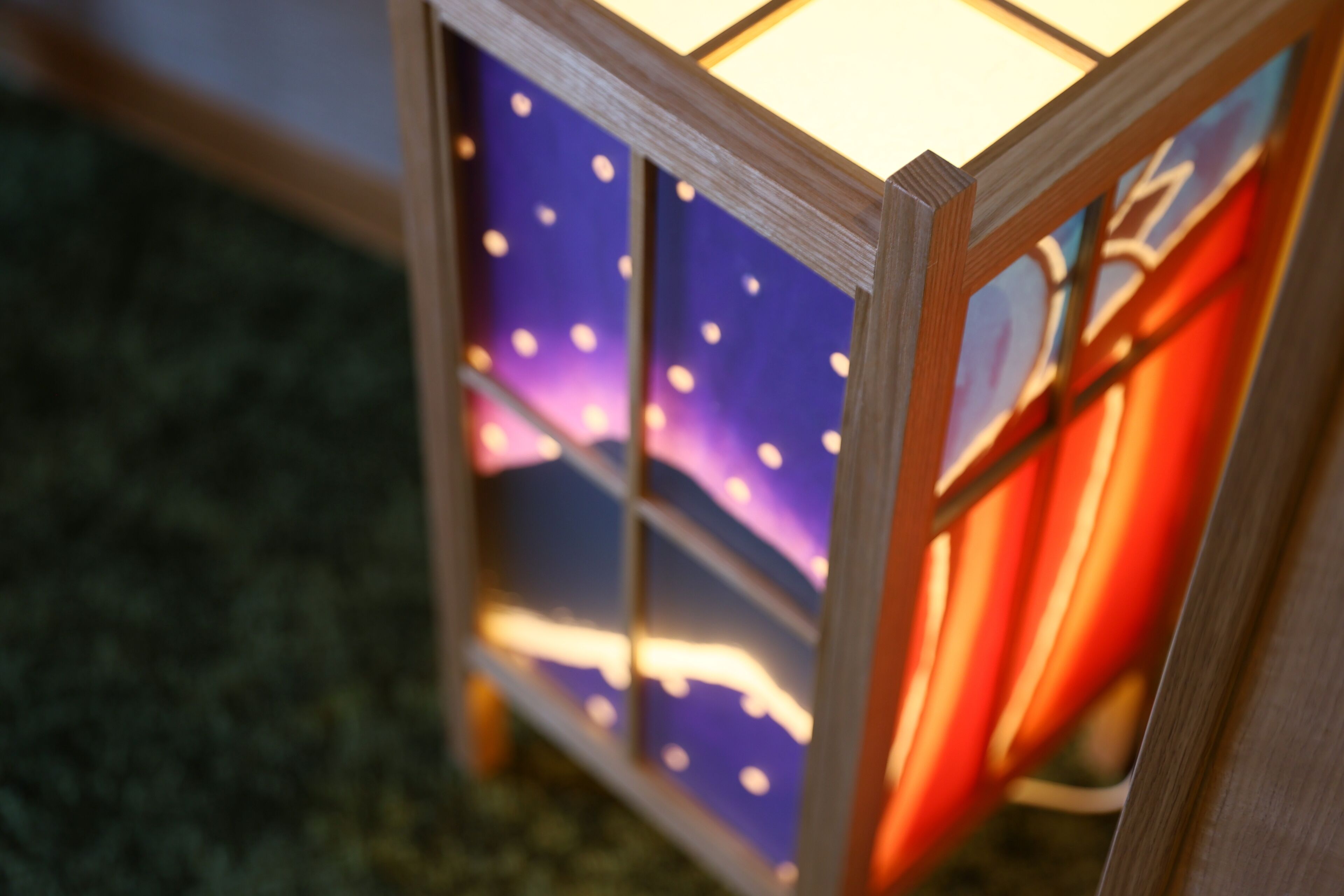 A close-up of a wooden lantern with a glass panel displaying a starry night scene.