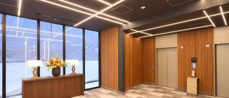 A modern lobby with a wooden reception desk, a large window, and an elevator.