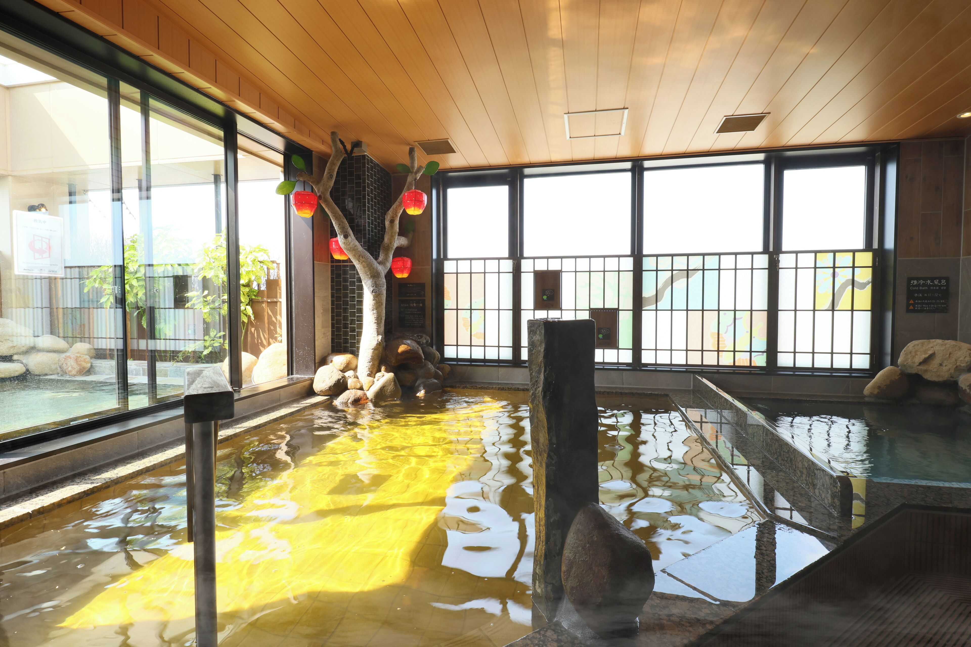 A large indoor pool with clear glass walls, wooden ceiling, and a view of the outdoors.