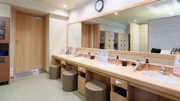A hotel bathroom with three sinks, a large mirror, and wicker stools.
