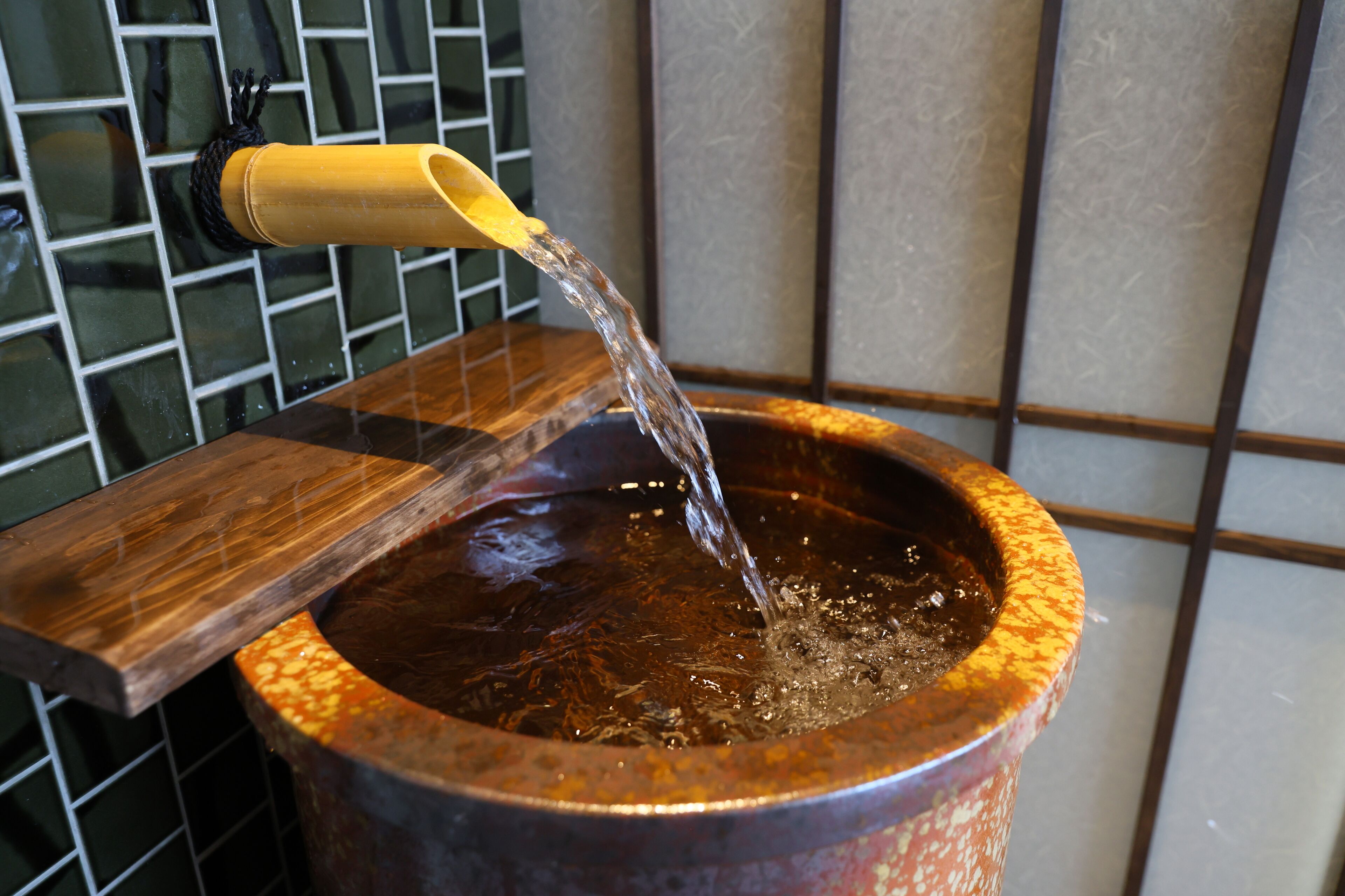 A stone basin with water flowing into it, a wooden tray, and a tiled wall in the background.