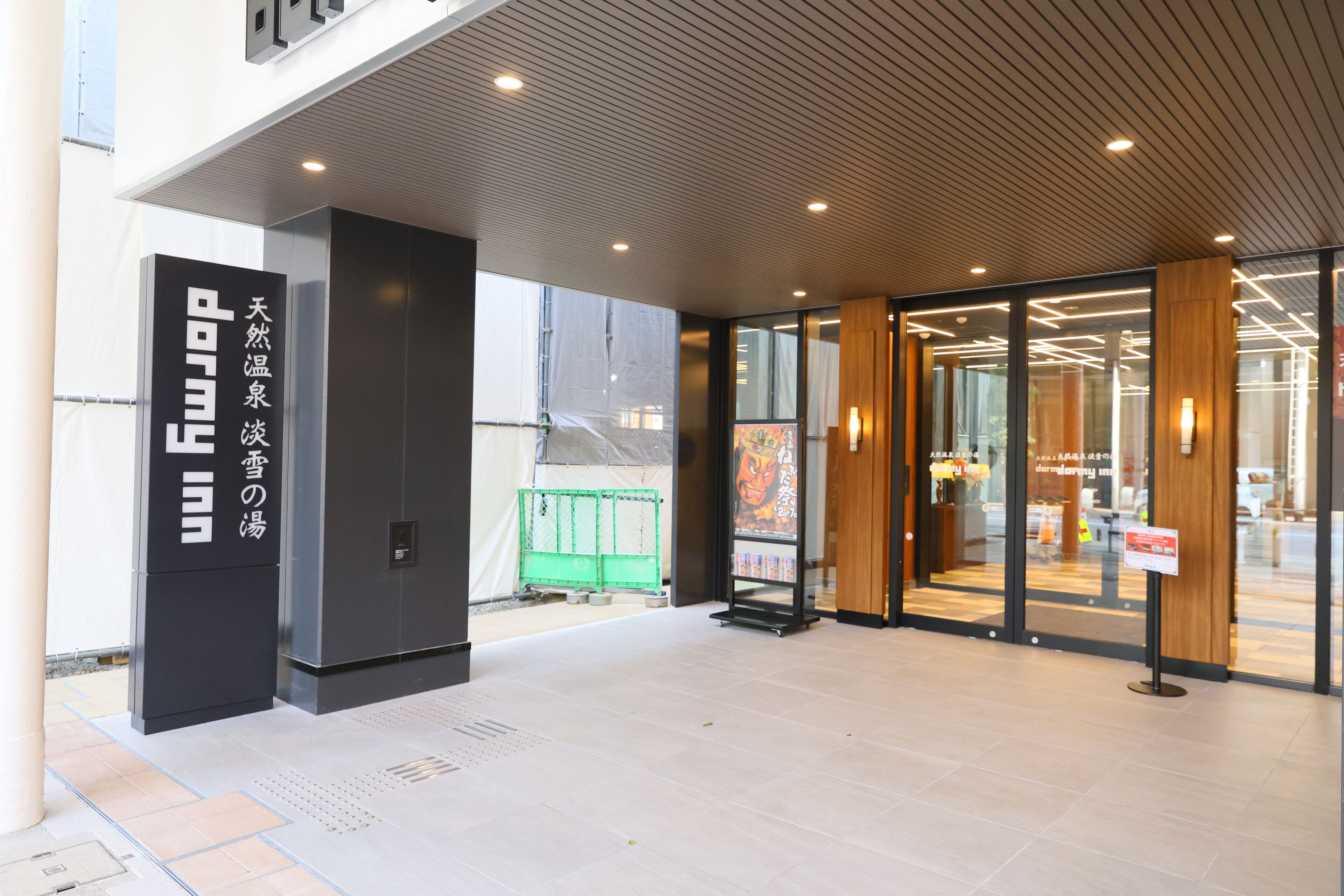 A modern building entrance with glass doors, a sign with Japanese characters, and a tiled floor.
