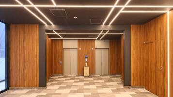 Un'area ascensore moderna con rivestimenti in legno, pavimento a parquet a spina di pesce e una colonna centrale con una targa.