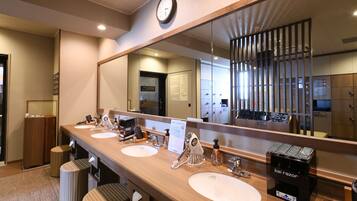 A hotel bathroom with three sinks, a large mirror, and a clock on the wall.