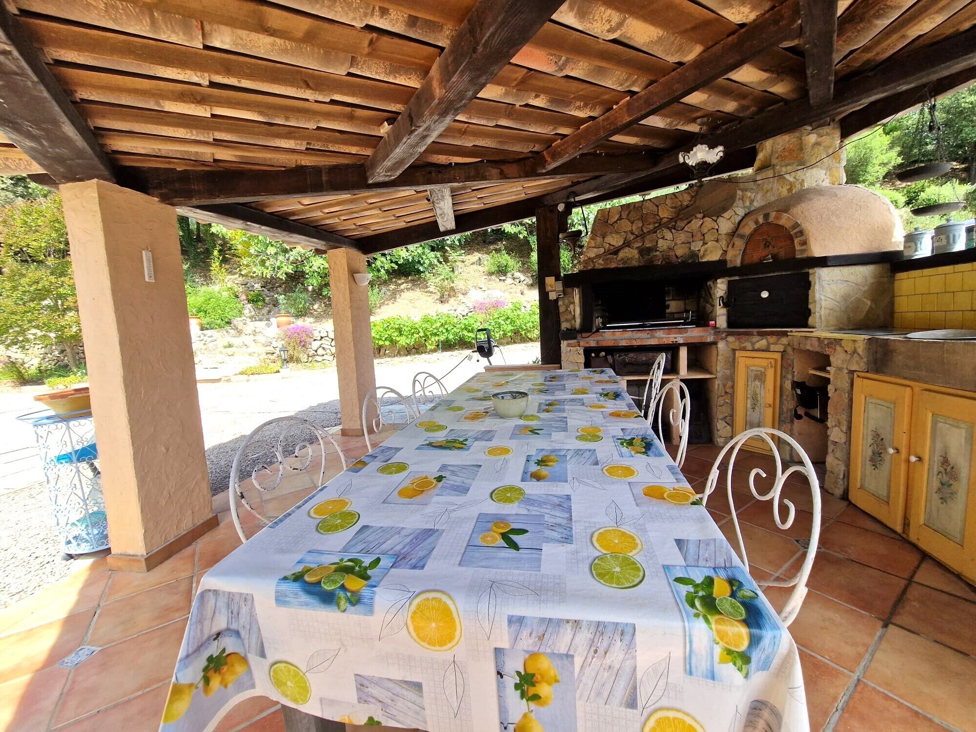An outdoor patio with a table covered in a lemon pattern tablecloth, surrounded by white metal chairs.