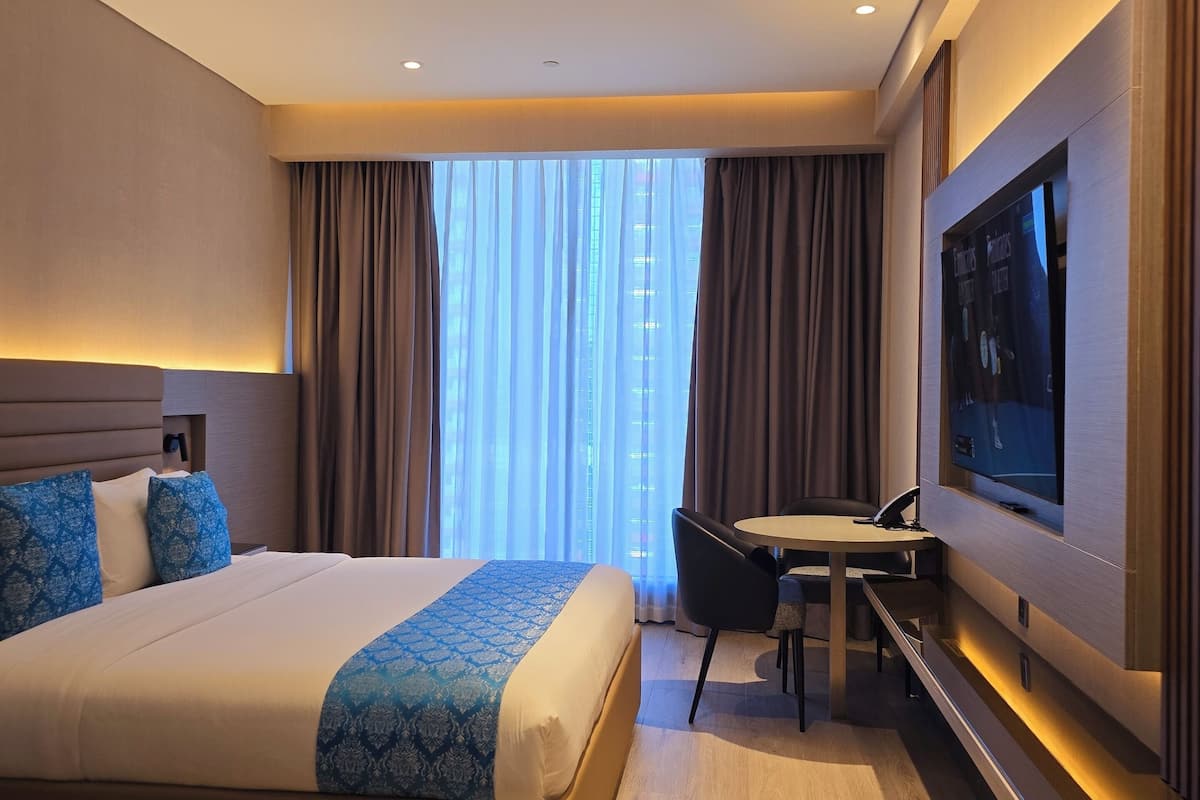 A modern hotel room with a large bed, a desk, and a television.