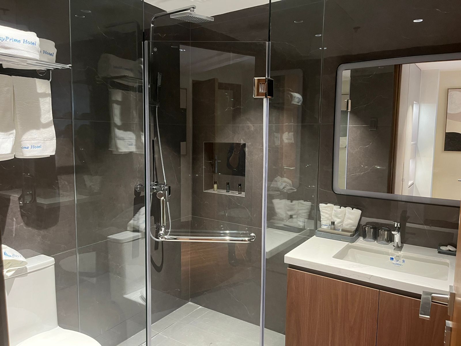 Een moderne badkamer met een douche in een glazen cabine, een wastafel met spiegel en toiletartikelen.