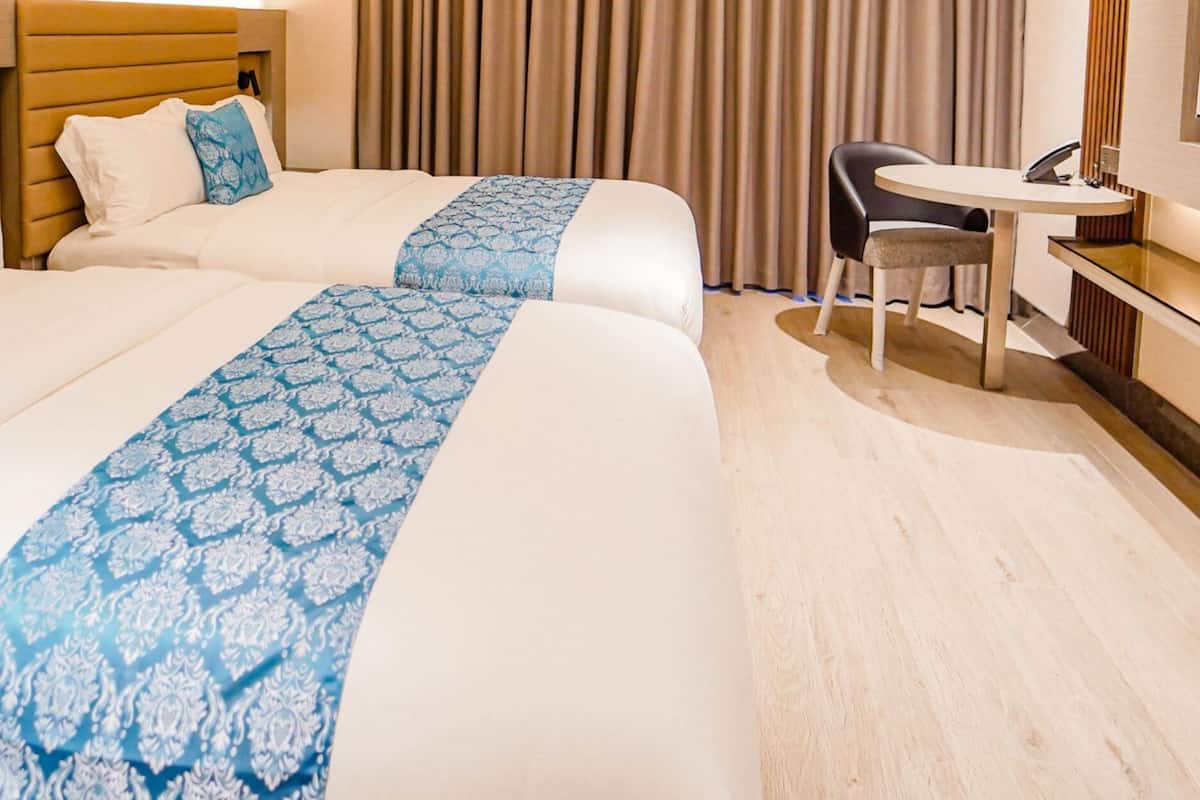 A hotel room with two beds, a small round table, a chair, and a TV.