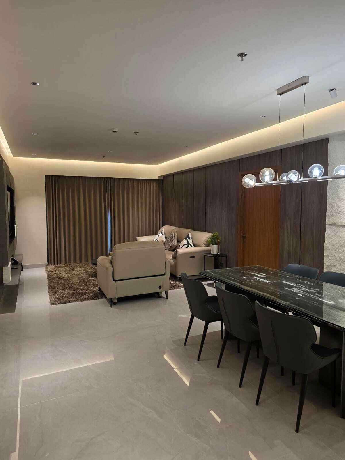 A modern dining area with a marble table and black chairs, a sofa, and a ceiling light fixture.