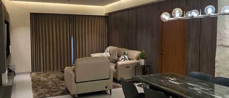 A modern dining area with a marble table and black chairs, a sofa, and a ceiling light fixture.