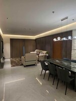 A modern dining area with a marble table and black chairs, a sofa, and a ceiling light fixture.