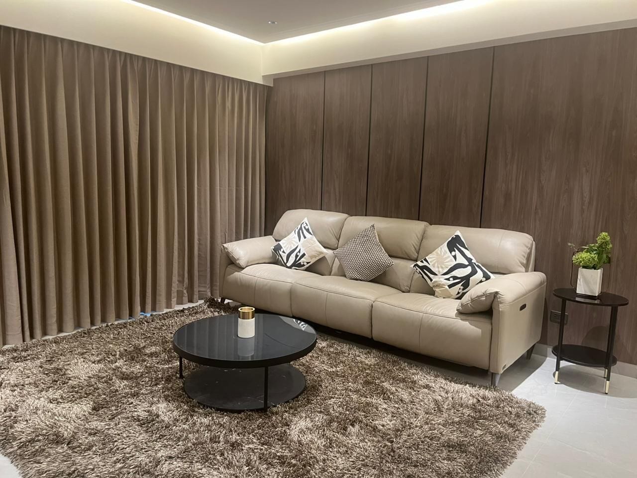 Uma sala de estar moderna com sofá, mesa de centro redonda e uma pequena mesinha lateral com uma planta.
