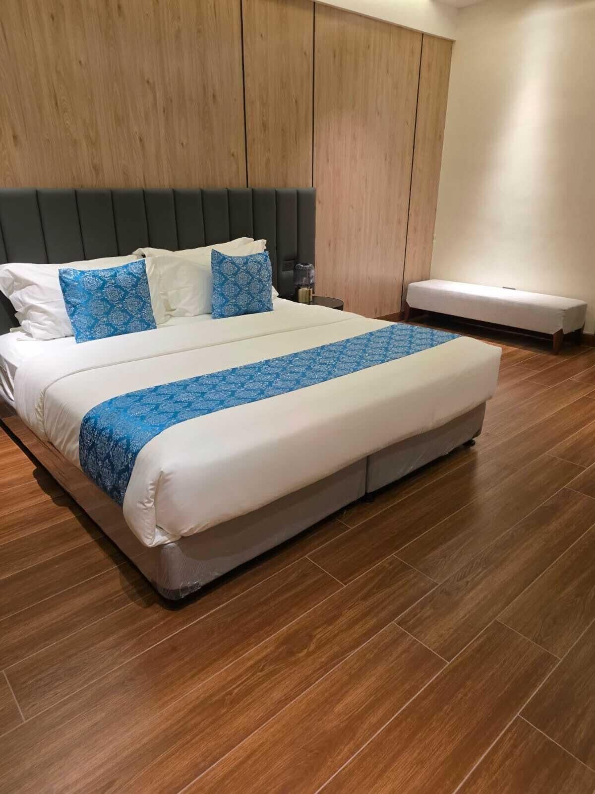 A large bed with a headboard, a bench, and a wooden floor.