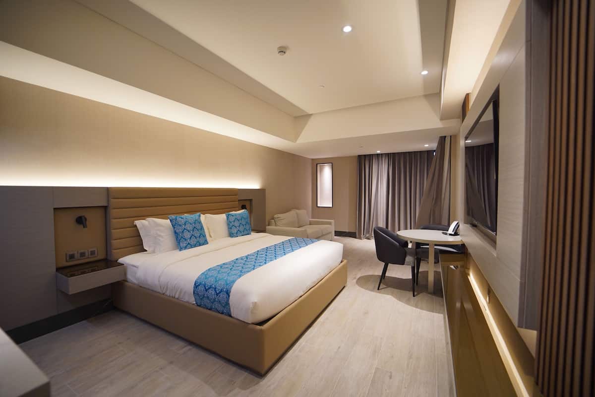 A modern hotel room with a large bed, a desk, and a chair.