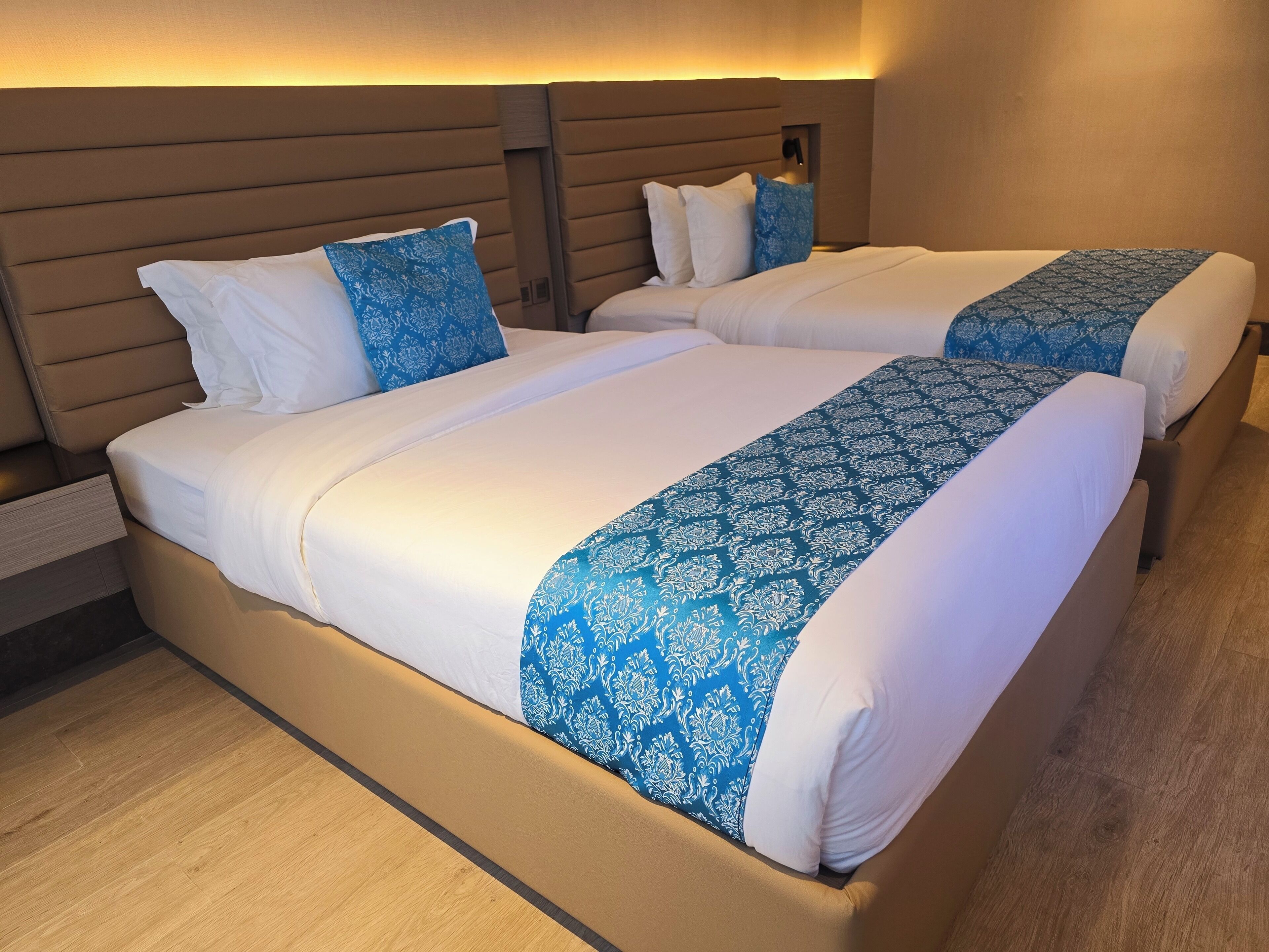A double bed with white and blue linens, a wooden headboard, and a bedside table.