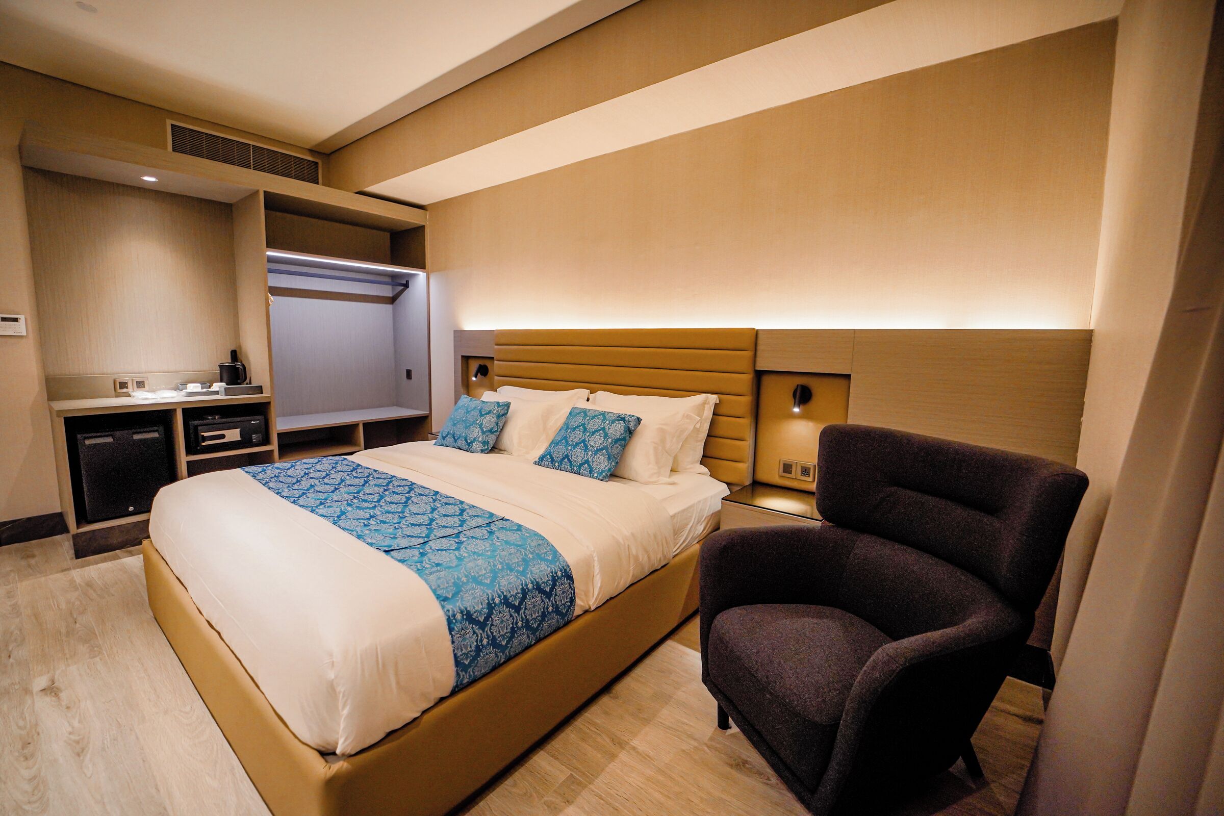 A hotel room with a large bed, a chair, a desk with a computer, and a TV.