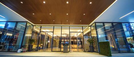 A modern building entrance with glass doors, a wooden ceiling, and a tiled floor.