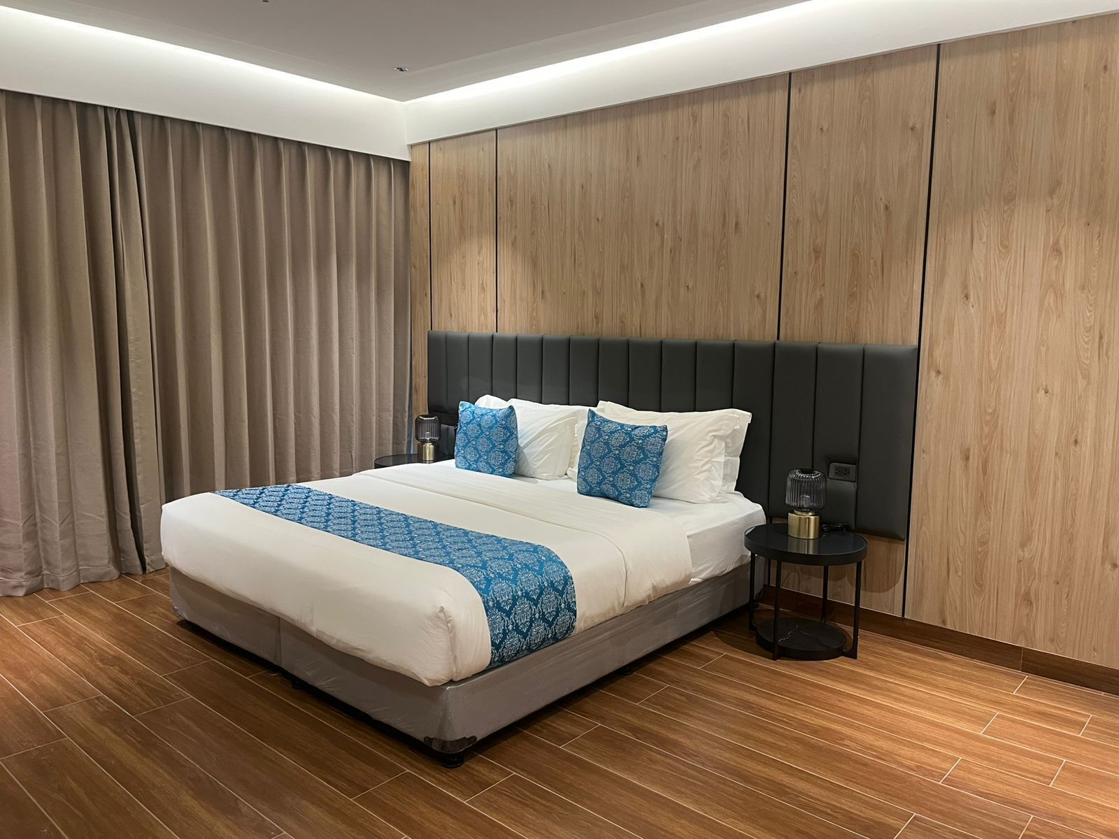A hotel room with a large bed, a nightstand, a lamp, and a wooden wardrobe.