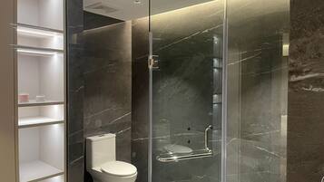 A modern bathroom with a glass-enclosed shower, a toilet, and a built-in shelving unit.