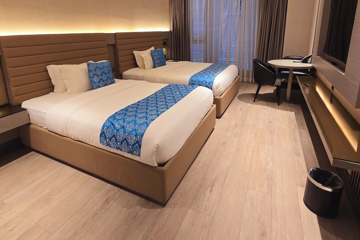 A hotel room with two beds, a desk, a TV, and a trash bin.