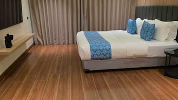 Een moderne hotelkamer met een groot bed, houten vloer, een flatscreen televisie en een groot raam met gordijnen.