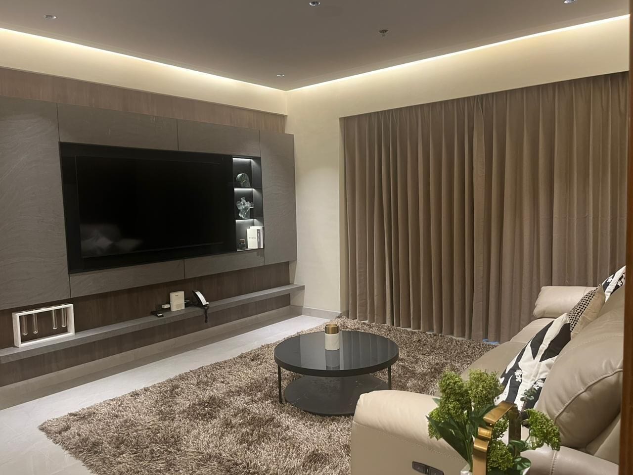 A modern living room with a flat-screen TV, a round coffee table, and a sofa.