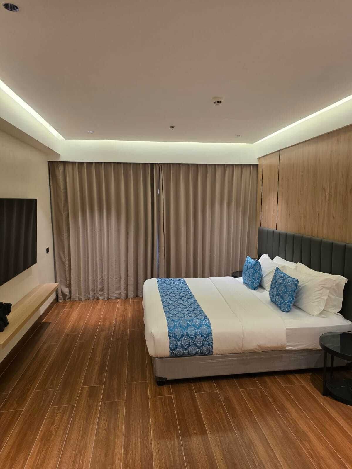 A hotel room with a bed, curtains, a bench, and a TV.