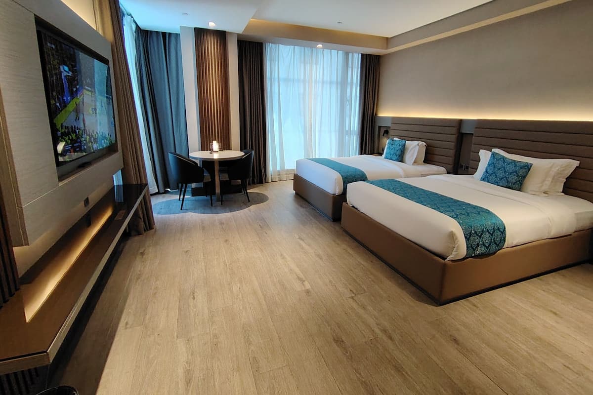 A hotel room with two beds, a TV, a small table, and a window with curtains.