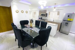 Una cuina moderna amb una illa central, electrodomèstics d'acer inoxidable i una zona de menjador amb taula de vidre i cadires negres.