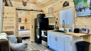 Een compacte kamer met houten lambrisering, een kitchenette, een bed en een televisietoestel dat wildlife toont.