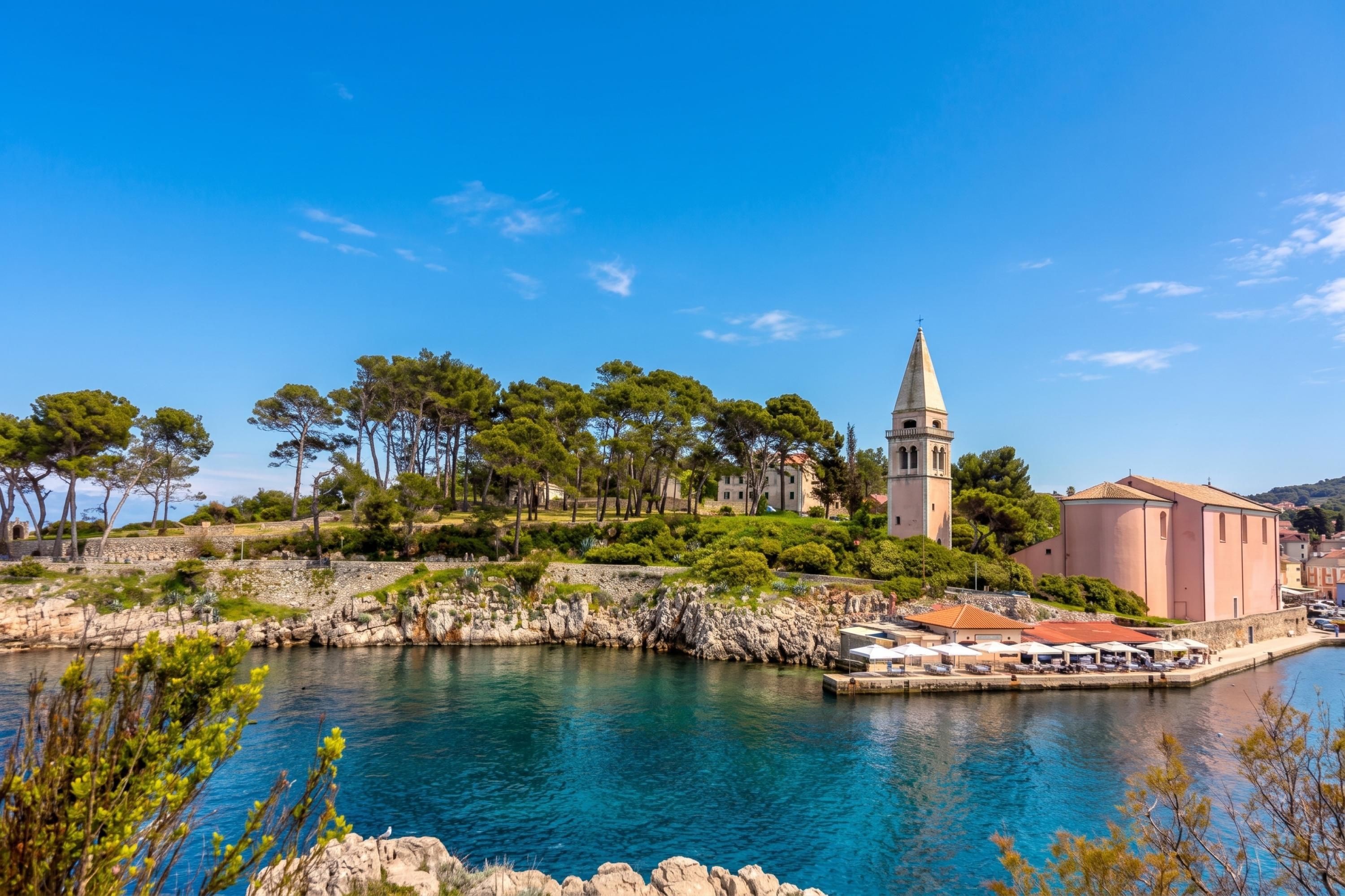 Una località costiera con un'imponente torre campanaria, una passeggiata lungomare e un litorale roccioso.