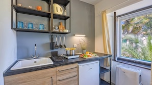 Cocina compacta con pileta, horno integrado y ventana con vista a palmeras.