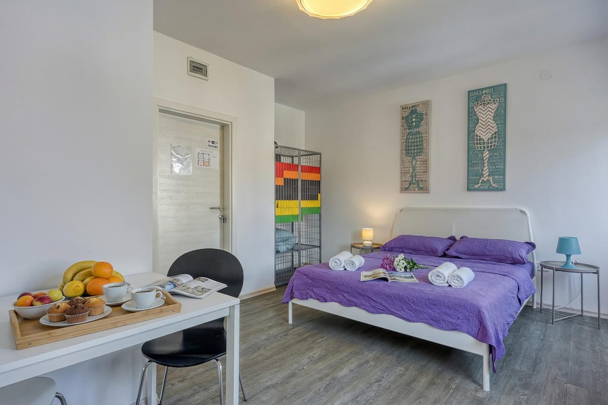 A bedroom with a bed, a desk with breakfast, and a door leading to a balcony.