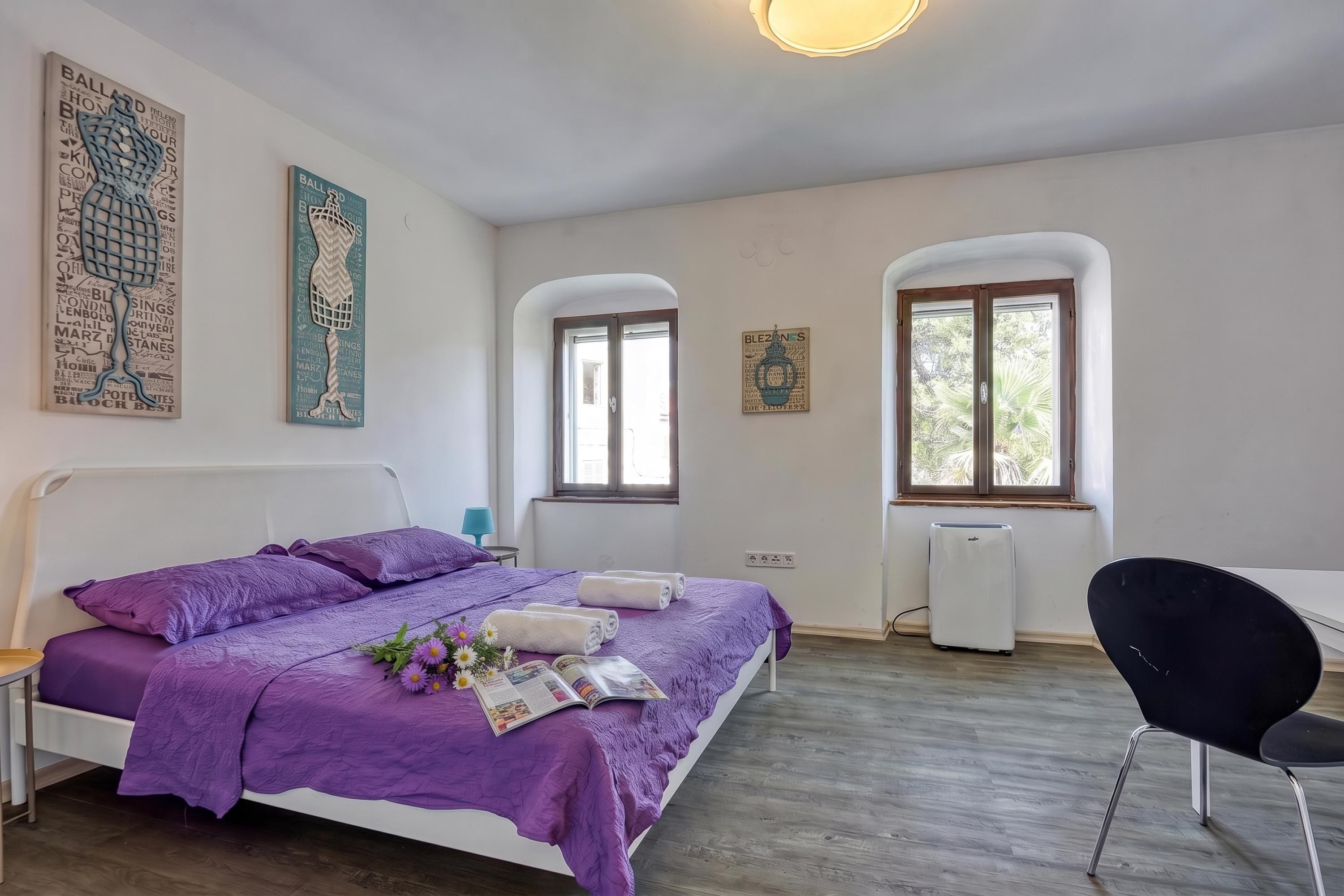 Un dormitorio con cama, escritorio y silla. Cuenta con dos ventanas y un radiador.