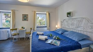 Un dormitorio ordenado con cama, mesita de noche, lámpara y ventana con cortinas.