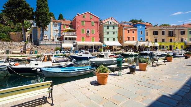 Un puerto con edificios coloridos, barcos amarrados y un paseo marítimo adoquinado.
