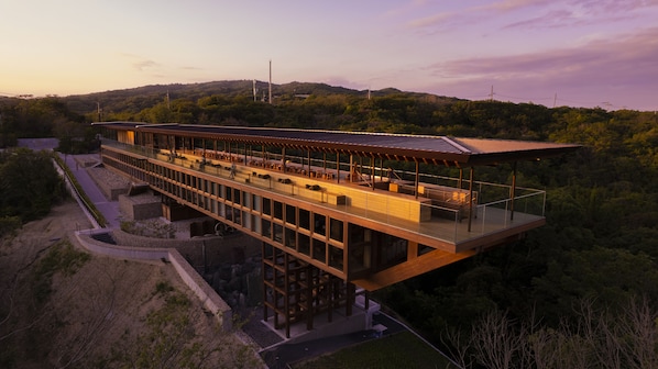 Un bâtiment moderne doté d’une façade en verre, de plusieurs étages et d’espaces extérieurs aménagés pour s’asseoir.