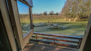 A wooden deck with a metal railing overlooking a grassy field with trees and a picnic table. - The Oak Hut (Whitchurch)