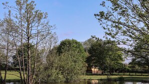 A tranquil pond surrounded by trees and a wooden fence. - The Oak Hut (Whitchurch)