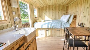 A wooden cabin interior with a bed, a sink, and a dining area. - The Oak Hut (Whitchurch)