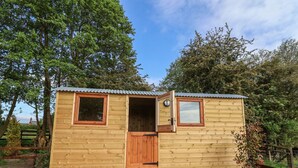 A wooden cabin with a door, windows, and a small porch. - The Oak Hut (Whitchurch)