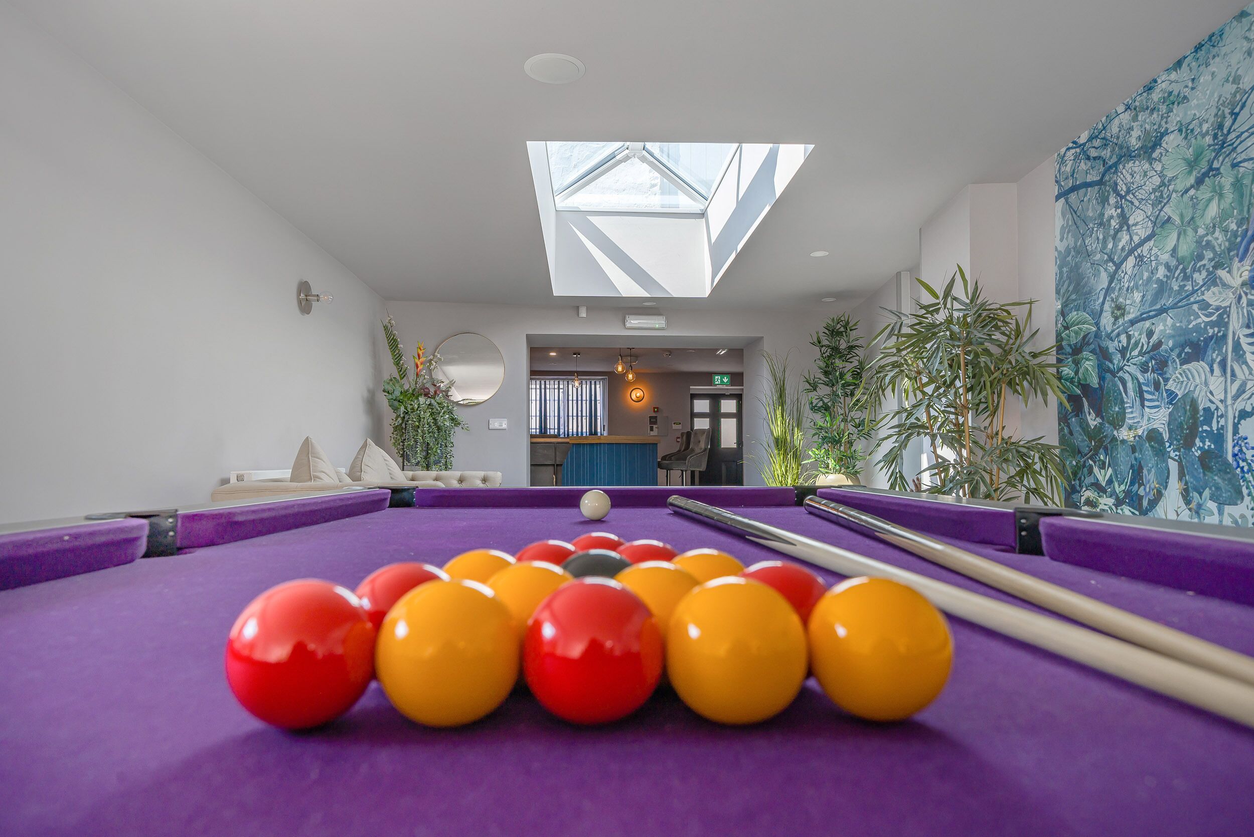 A pool table with balls, a skylight, and a mural.