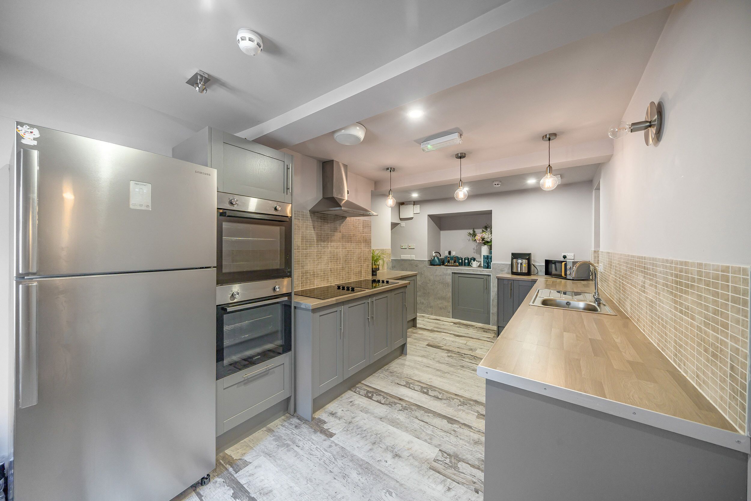 A modern kitchen with stainless steel appliances, grey cabinets, and a wooden countertop.