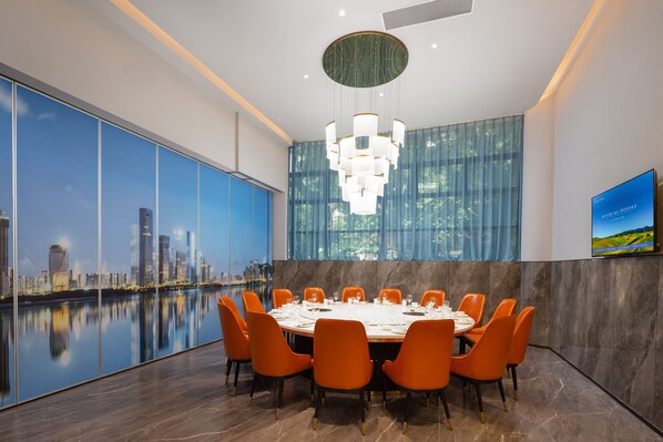 Une salle de conférence moderne offrant une vue panoramique sur la ville, une table ronde préparée pour une réunion et un grand lustre.