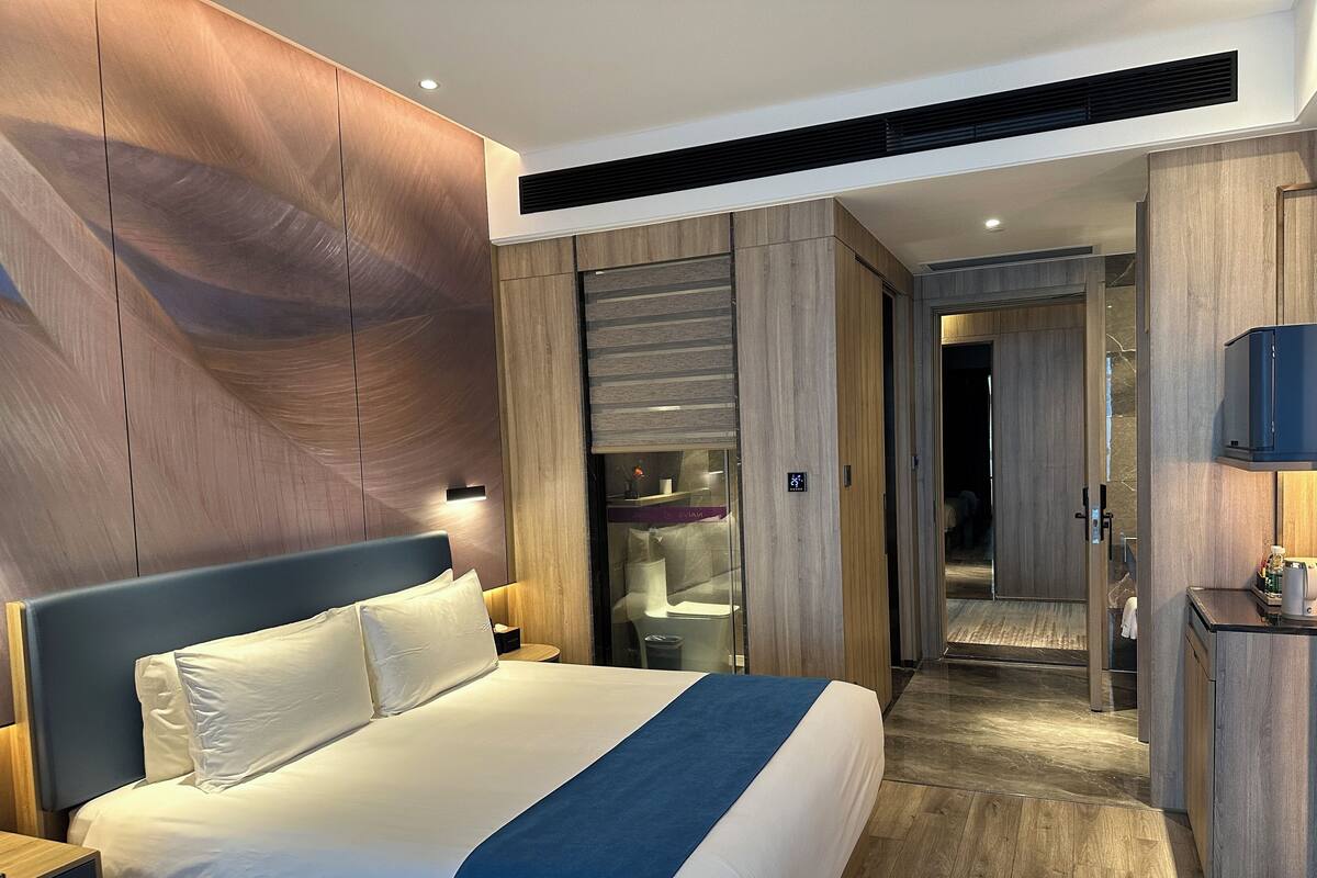 A modern hotel room with a large bed, wooden panel walls, a built-in TV, and a walk-in closet.