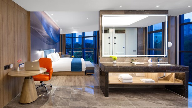 A modern hotel room with a bed, a desk with a laptop, a large bathroom vanity, and a large window offering a city view. - Shenzhen Naive S Hotel (Xili Metro Station Store) (Shenzhen)