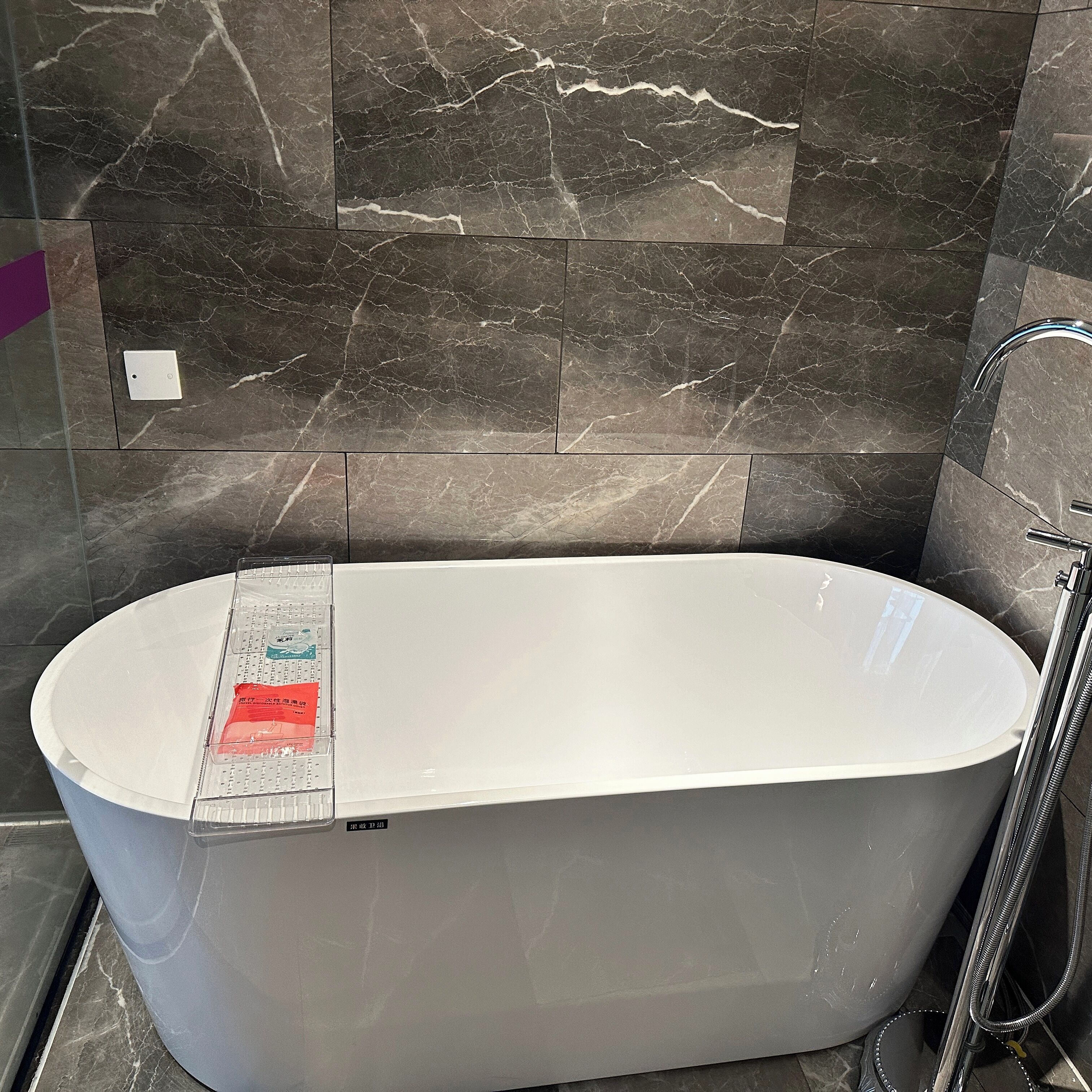 A modern bathroom with a freestanding bathtub, a shower area, and dark marble tiles.