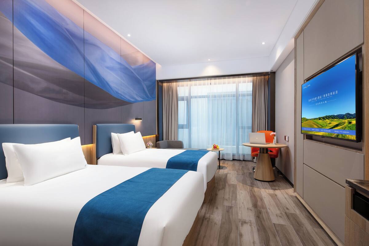 A hotel room with two beds, a TV, a desk, and a view of the outdoors.