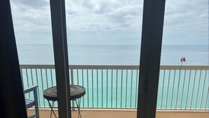Een balkon met een tafel en stoel, een witte balustrade en uitzicht op zee.